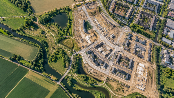 Luchtfoto van een woonwijk in ontwikkeling, omringd door bestaande bebouwing, infrastructuur, water en groen.